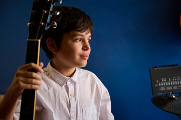 Confident portrait of a dark haired Caucasian teenager boy, a musician guitarist in white shirt,...