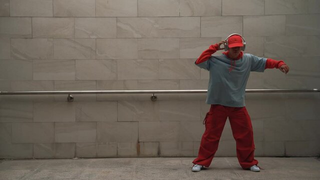 Handsome choreographer practice street dance in gray background. Young attractive b boy dancer perform while wearing stylish cloth. Feeling of lively step. Copy space. Outdoor sport 2024. Sprightly.