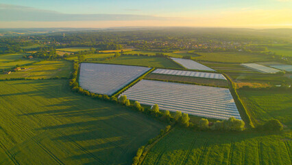 AERIAL: Golden sunset light shines on greenhouses amidst lush farming fields