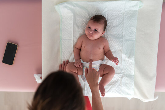 Top view of mother changing diaper of her newborn baby lying on bed