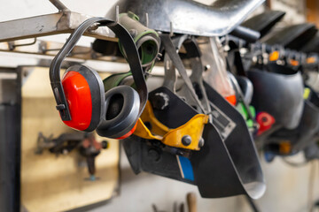 Welding helmets, protective glasses, ear protection hung in a row in a welding workshop - obrazy, fototapety, plakaty