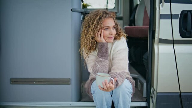 Camping woman holding mug with beverage sitting camper van stairs at vacation