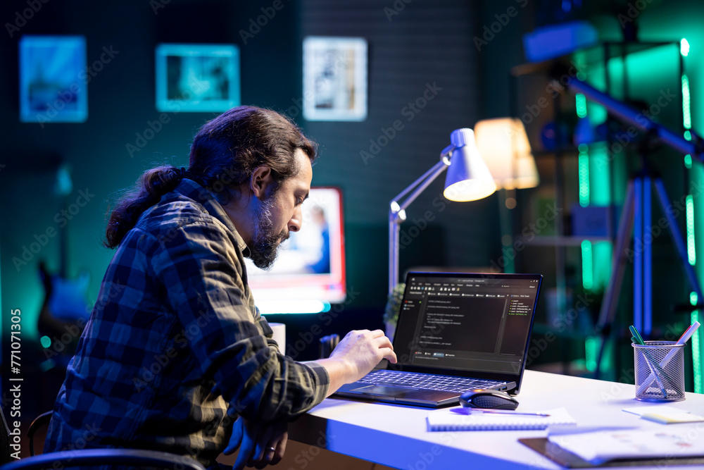 Poster dedicated male programmer uses his portable computer to manage databases and keep an eye on network 