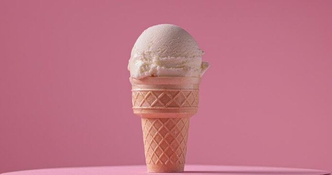 vanilla ice cream in waffle cone turning on pink background