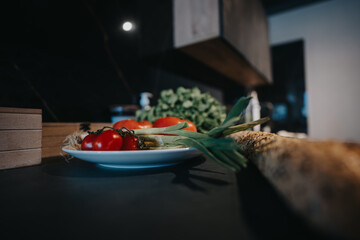 A plate of ripe tomatoes and fresh vegetables alongside crusty bread on a dark counter top...