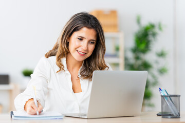 Adult blonde woman taking notes while working from home