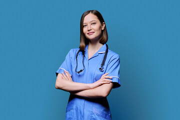 Portrait of young female nurse looking at camera on blue background