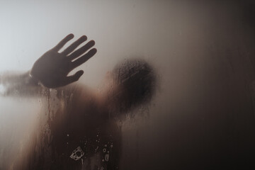 Mysterious silhouette of a person seen through a misted glass surface with a clear hand print.