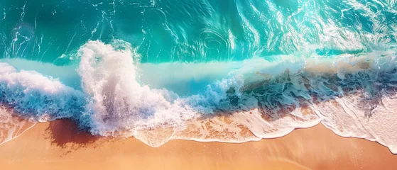 Deurstickers A stunning high-angle shot captures the dynamic interaction between a powerful turquoise wave and the sandy beach © Daniel