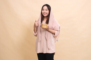 cheerful asian muslim woman winking forward hand gesture thumbs up okay good and wooden bowl in front of chest containing delicious dimsum