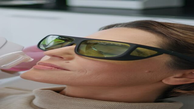 Beautician making facial treatment with laser device in clinic vertical closeup