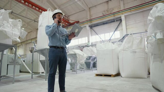 Chief engineer of pvc windows factory speaks on phone and using a laptop on production line