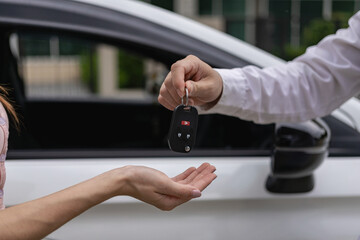 A young man receives keys from a car salesman. After agreeing to a lease or sale contract, buying a car and finance concept, close-up image - obrazy, fototapety, plakaty