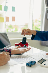 A young man receives keys from a car salesman. After agreeing to a lease or sale contract, buying a...