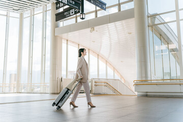空港・駅・ビル・公共交通施設でスーツケースを持って歩くビジネスウーマン（海外出張・徒歩）
 - obrazy, fototapety, plakaty