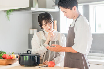 スマホを見ながらキッチンで料理を作る夫婦（レシピサイト・レシピアプリ）
