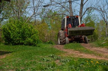 Naklejka premium A man driving a red tractor full of gravel in the bucket during spring on a sunny day