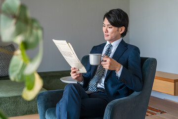朝家で英字新聞を読むスーツ姿のアジア人ビジネスマン

