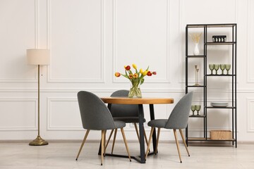Stylish dining room interior with comfortable furniture and beautiful tulips