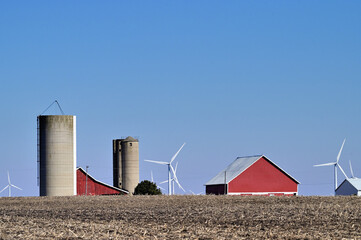 Barns, silos and wind  turbines make up an array of structures that rise above the earth in this...
