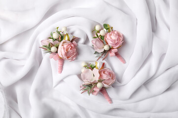 Stylish pink boutonnieres on white silk, flat lay
