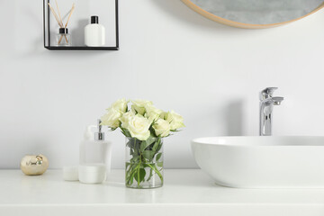 Bouquet of beautiful roses in vase and bath accessories near sink in bathroom