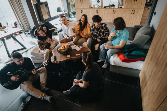 Casual indoor gathering of friends sitting comfortably, playing guitar, and having a good time
