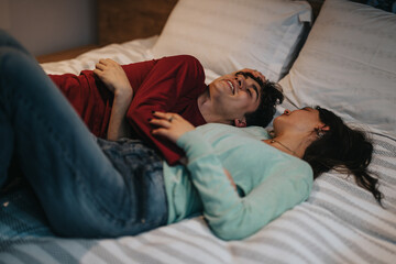 Affectionate young man and woman lying on a bed, sharing a joyful and intimate moment of...