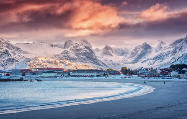Arctic sandy beach, blue sea and snowy mountains at sunset