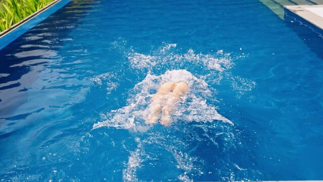 Woman dives into infinity pool at tropical villa, glides underwater in slow motion, surfacing in luxe setting. Relaxation, leisure at exclusive resort, clear blue water, private swim, upscale travel.