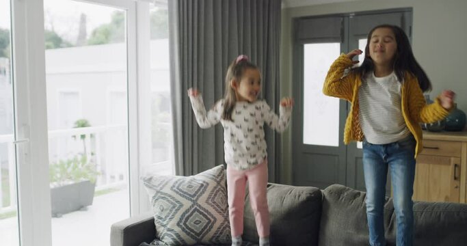 Sisters, kids and jump on sofa in home, playing game and having fun together. Siblings, energy and girls in action on couch, bonding or excited family bounce in celebration for freedom in living room
