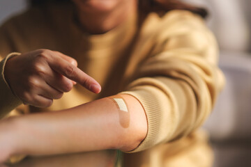 Closeup image of a young woman pointing finger at a adhesive bandage, medical plaster, band aid on her arm - obrazy, fototapety, plakaty
