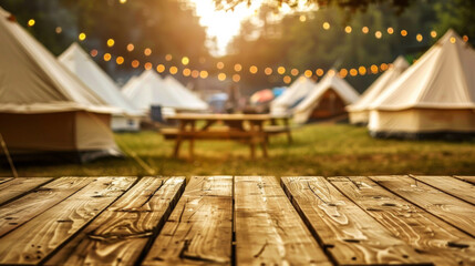 A wooden table overlooking the tents and several picnic tables. The tents are illuminated with lights, creating a warm and cozy atmosphere. Camping concept. - obrazy, fototapety, plakaty