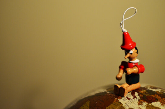 Wooden Pinocchio sitting on a round Earth decorative vintage globe just on top of Italy.