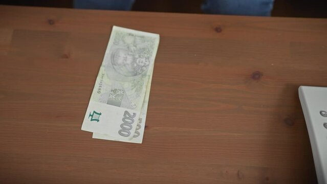 Hand placing a czech 2000 koruna bill on a wooden table, symbolizing finance, currency, and payment indoors.