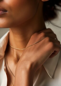 closeup woman wearing gold necklace white shirt thin straight lines pandora interconnections holding wiry protective shoulder long sold connections
