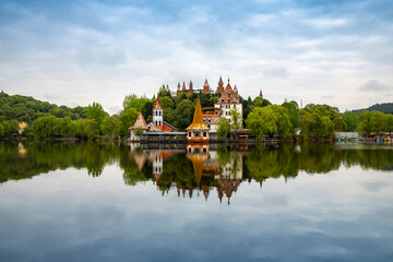 Fototapeta premium A group of ancient castle -style buildings are built in a small hillside forest, with a large lake outside, in a park in Deyang, China