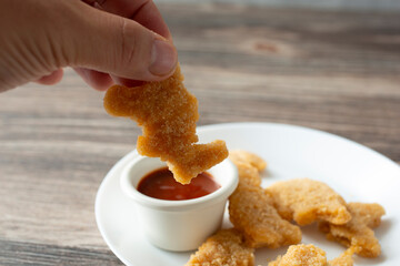 A view of a hand dipping a dino nugget into BBQ sauce.