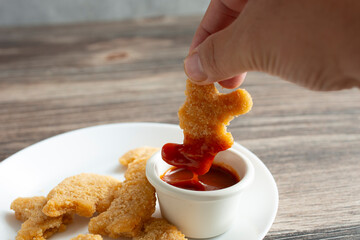 A view of a hand dipping a dino nugget into BBQ sauce.