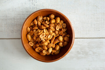 A top down view of roasted peanuts in a clay bowl.