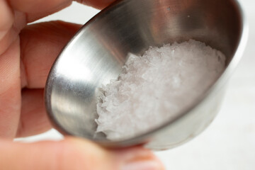 A view of a hand holding metal condiment cup of large sea salt flakes.