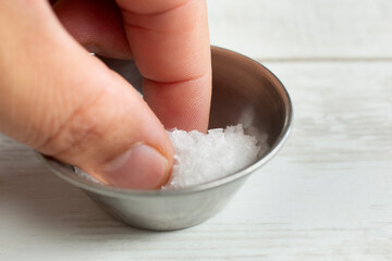 A view of a hand picking up some large sea salt flakes from a metal condiment cup.