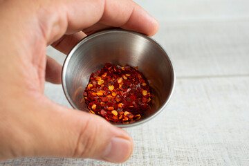 A view of a hand holding a metal condiment cup of crushed red peppers.