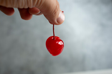 A view of a hand holding a maraschino cherry.