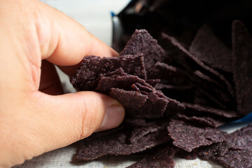 A view of a hand grabbing some blue corn tortilla chips.