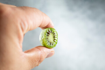 A view of fingers holding a kiwi berry half.