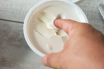 A top down view of a finger scooping some dairy-free cream cheese out of the package.