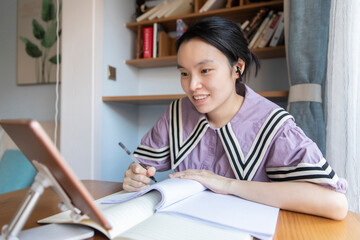 An Asian woman is studying diligently on a tablet in the living room desk at home