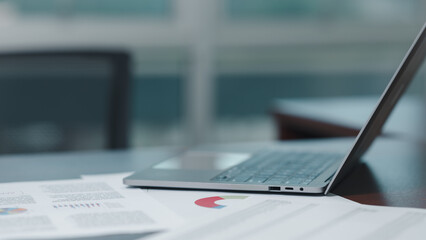 A laptop is open on a table with a stack of papers in front of it