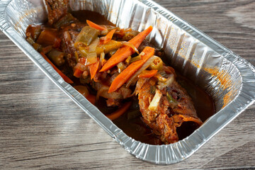 A closeup view of an aluminum container of brown stew fish.